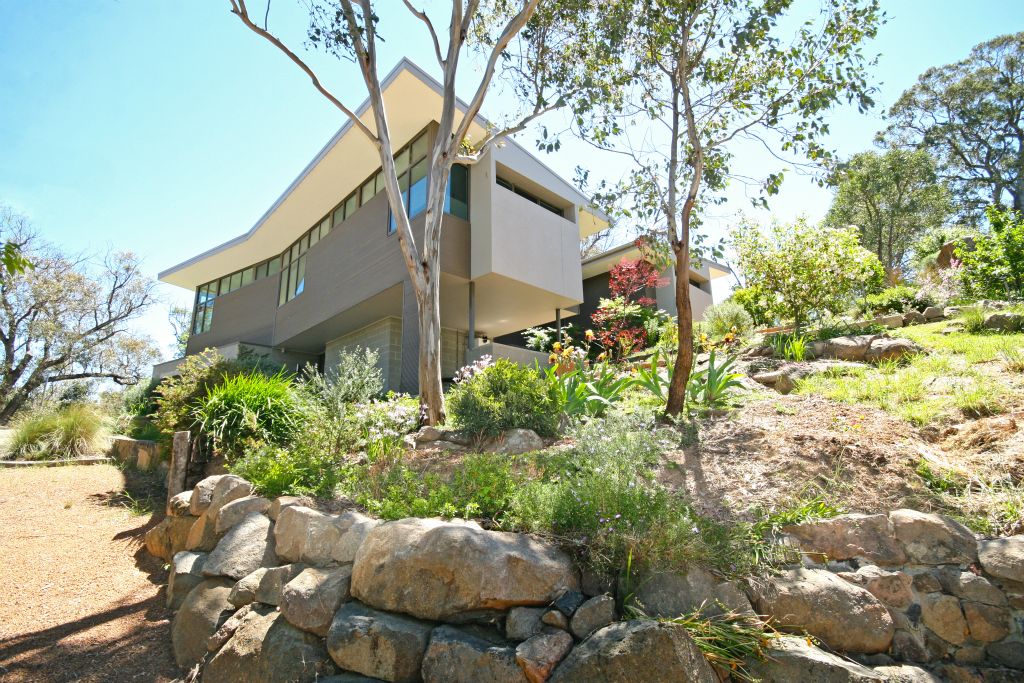 The  project involved the building of a new bush house in Wallaroo, NSW, on a sloping  block next to the Murrumbidgee   River.The  design comprises 2 wings connected by a central link. Both wings are oriented  to maximise the northern aspect and to enjoy the panoramic views. The North wing  (living) floats over the land and is linked to the garden with two bridges. The  South wing (bedrooms and study) sits above the house entry and garage and has  tranquil views of the river. Between the wings is a cantilevered deck  overlooking an amphitheatre of hills.Each  wing has a sculpted quality through its roof profile, pop-out walls, and by the  use of contrasting materials. Their exterior form is mirrored internally where  the flat ceiling splits to a rake over the windows as a gesture towards the  hills, tree canopy and the sky. The effect from inside is of a light-filled  space with a close connection to the surrounding bush.The  joinery is treated as another element that is integrated with the architecture.  The interior finishes are a mixture of white walls, timber and stone. They are  used with restraint to reinforce the clean lines and minimalist character of  the spaces.