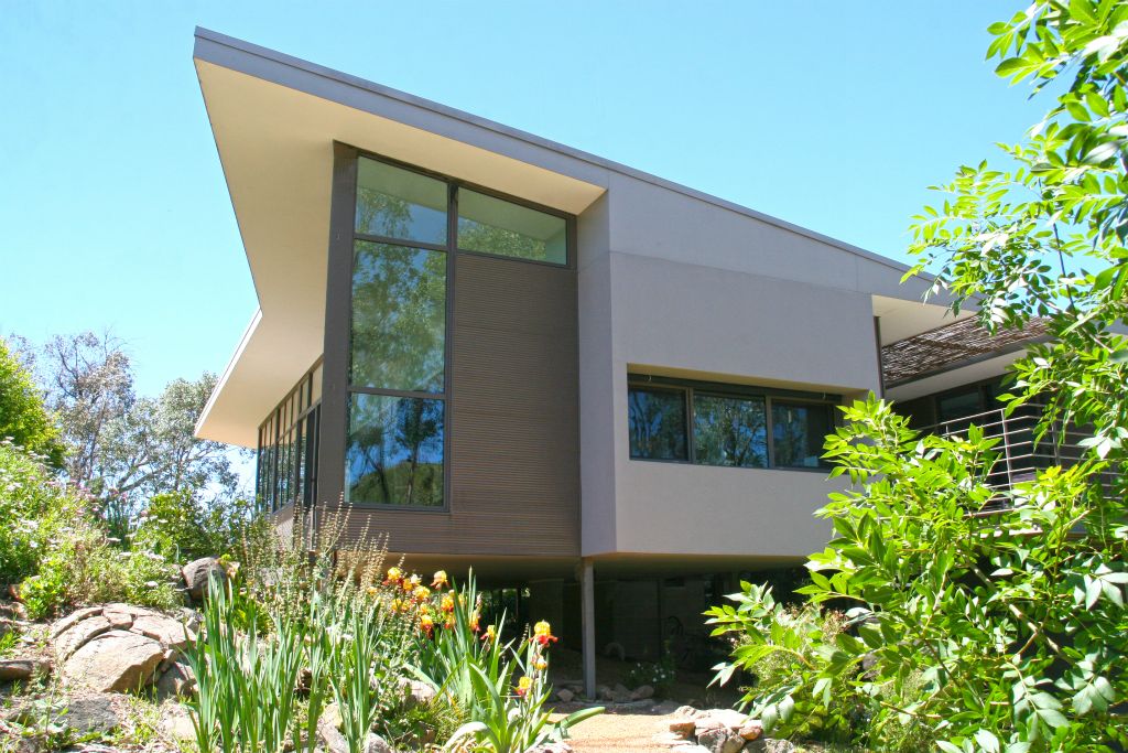 The  project involved the building of a new bush house in Wallaroo, NSW, on a sloping  block next to the Murrumbidgee   River.The  design comprises 2 wings connected by a central link. Both wings are oriented  to maximise the northern aspect and to enjoy the panoramic views. The North wing  (living) floats over the land and is linked to the garden with two bridges. The  South wing (bedrooms and study) sits above the house entry and garage and has  tranquil views of the river. Between the wings is a cantilevered deck  overlooking an amphitheatre of hills.Each  wing has a sculpted quality through its roof profile, pop-out walls, and by the  use of contrasting materials. Their exterior form is mirrored internally where  the flat ceiling splits to a rake over the windows as a gesture towards the  hills, tree canopy and the sky. The effect from inside is of a light-filled  space with a close connection to the surrounding bush.The  joinery is treated as another element that is integrated with the architecture.  The interior finishes are a mixture of white walls, timber and stone. They are  used with restraint to reinforce the clean lines and minimalist character of  the spaces.